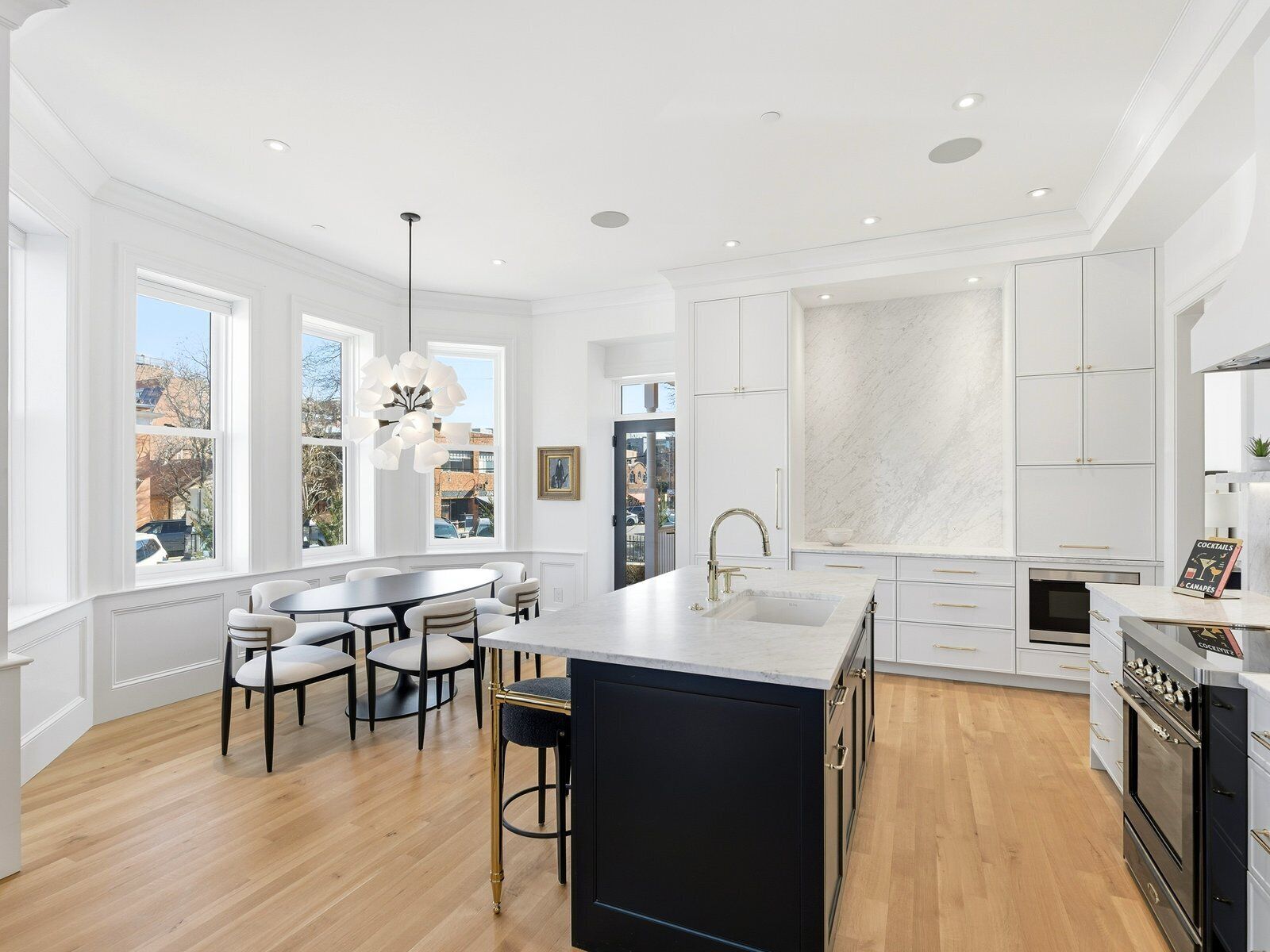 A modern kitchen with a large island, white cabinetry, and a view of the city through large windows.