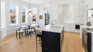 Een moderne keuken met een groot eiland, witte kasten en een stadszicht door grote ramen.