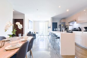 Una cocina moderna con una isla central, taburetes de bar y una zona de comedor con una mesa preparada para dos.