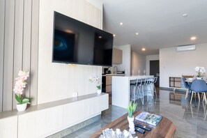 Una sala de estar moderna con un televisor de pantalla plana en la pared, una cafetera y un comedor con taburetes de bar.