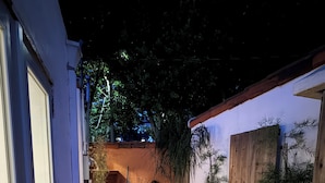 Une terrasse en bois mène à un bâtiment doté d’une porte blanche, qui est entouré de plantes en pot et d’une clôture en bois.