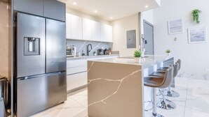 Een moderne keuken met een roestvrijstalen koelkast, witte kasten, een marmeren eiland en barkrukken.