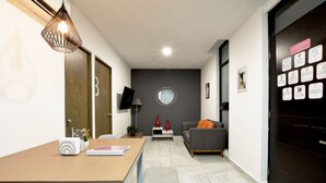 Un soggiorno moderno con un divano grigio, un tavolino in legno e un televisore montato a parete. Si nota una porta nera con una bacheca sul lato destro.