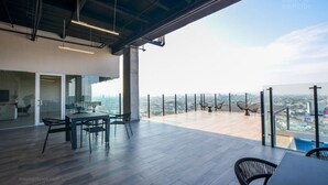 A modern office space with a panoramic city view, featuring a glass partition, a dining area, and a high ceiling with exposed beams.