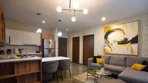 A modern kitchen with a central island, a dining area with chairs, a sofa with cushions, and a large abstract painting on the wall.