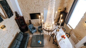 A cozy room with a stone wall, a sofa, a table with candles, and a chandelier. - Suite Ravenna : Charm, Cathedral height & Luxury, Swimming pool - Domaine de Pagnon (Saint-Gervais)