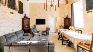 A spacious living room with a leather sofa, two armchairs, a dining table with chairs, a chandelier, and stone walls. - Suite Ravenna : Charm, Cathedral height & Luxury, Swimming pool - Domaine de Pagnon (Saint-Gervais)