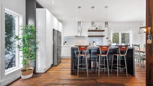 Une cuisine moderne dotée d’un îlot central, de tabourets de bar, d’un réfrigérateur et d’une plante en pot.