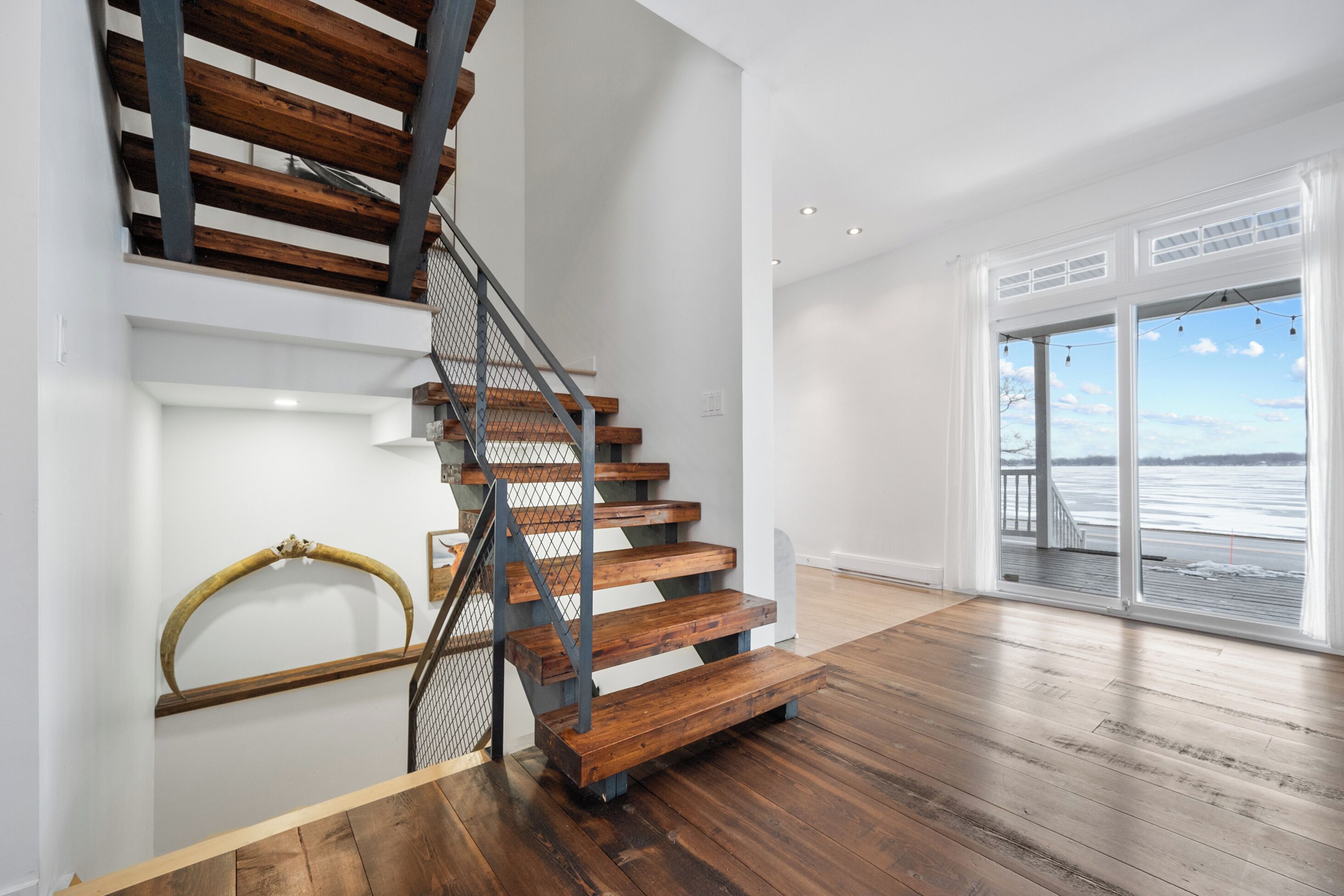 A staircase with wooden steps and metal railings, leading to a room with a large window overlooking a body of water.