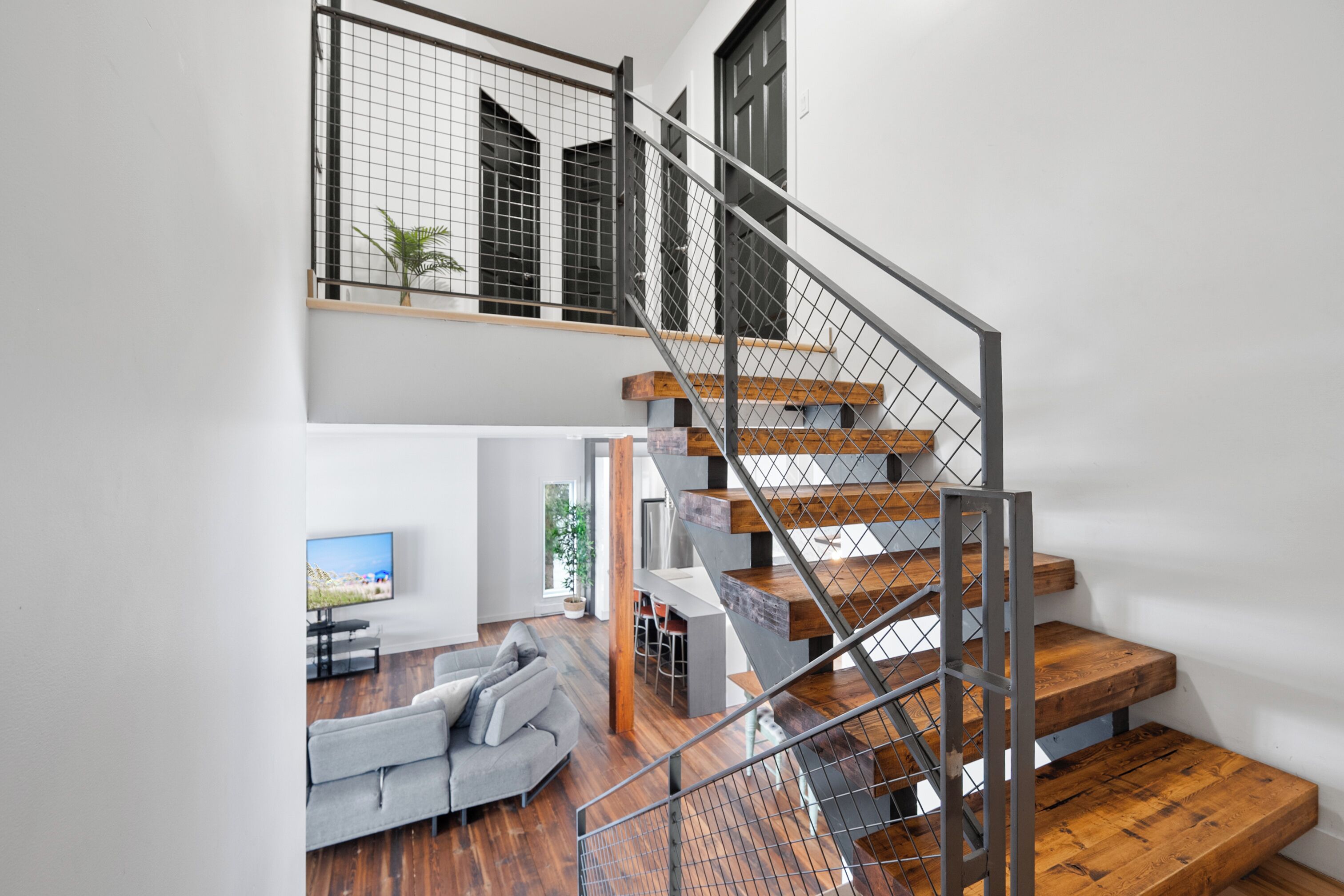 Un interior moderno con una escalera de madera, un sofá gris y un televisor de pantalla plana.