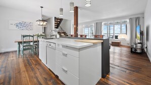 Une cuisine moderne dotée d’un îlot central, de planchers en bois et de luminaires suspendus.