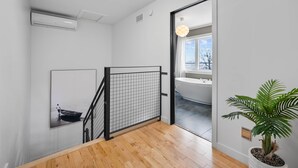 Un intérieur moderne avec un escalier en bois, une plante en pot et une vue sur une salle de bain à travers une porte en verre.