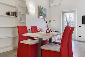 A dining area with a white table, red chairs, a vase with flowers, and a bookshelf with books and a vase. - Apartment 'Azalea' with Lake View, Wi-Fi and Air Conditioning (Laveno-Mombello)