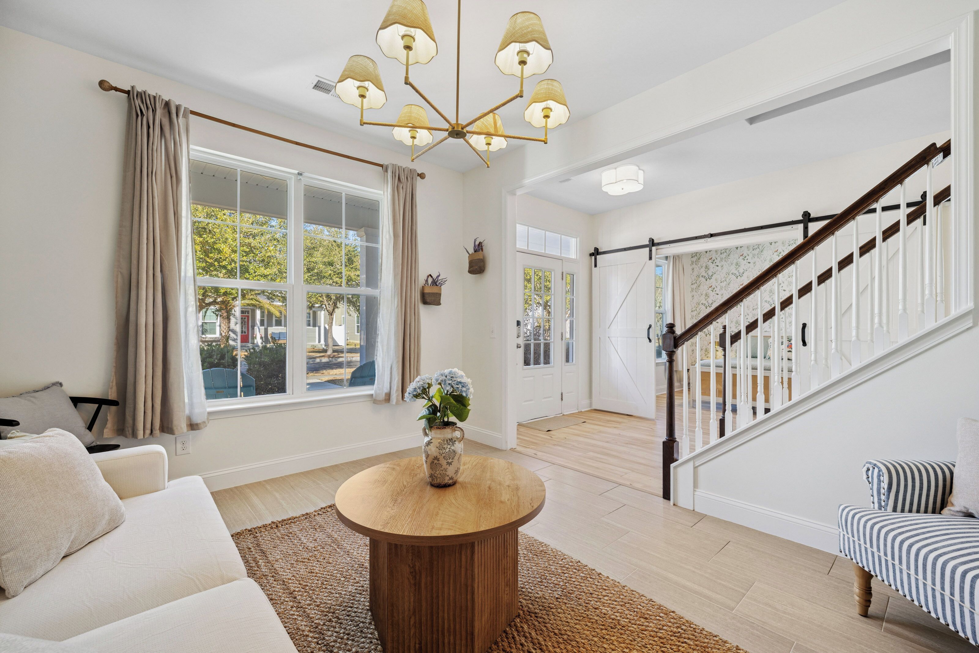 Ein geräumiges Wohnzimmer mit einem runden Couchtisch, einer Couch, einer Treppe mit Holzbalkon und einem großen Fenster mit Vorhängen.