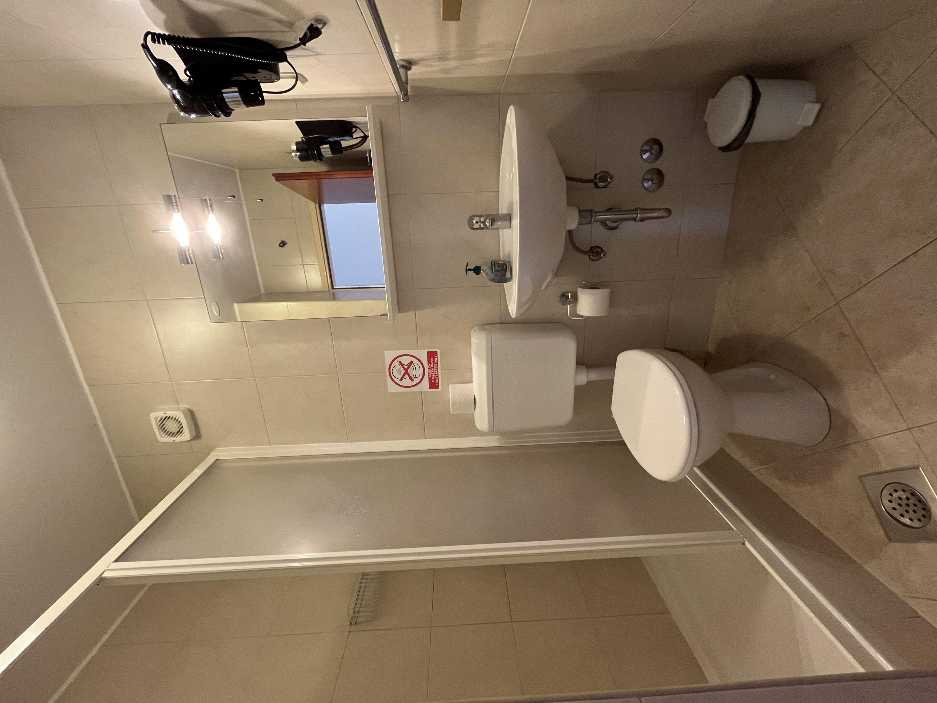 A bathroom with a toilet, sink, mirror, and a no-smoking sign.