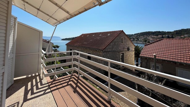 A balcony with a view of a coastal town, a stone building with a red-tiled roof, and a clear blue sky. - Cozy 1-bedroom apartment in quaint Lumbarda with AC (Lumbarda)