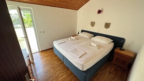 Un dormitorio con techo de madera, una cama con ropa blanca, una mesita de noche y vistas a través de un ventanal abierto.