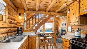 Ein Blockhaus-Interieur mit Küche, Holztreppe und Kamin aus Stein.