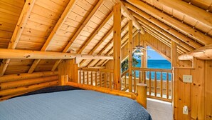 Eine Holzhütte mit Bett, einem Balkon mit Meerblick und einem sichtbaren Holzbalkengerüst.