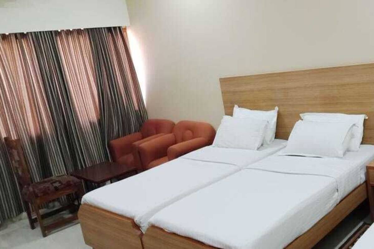 Habitación de hotel con dos camas, cabecero de madera, una mesita, una silla y una cortina.