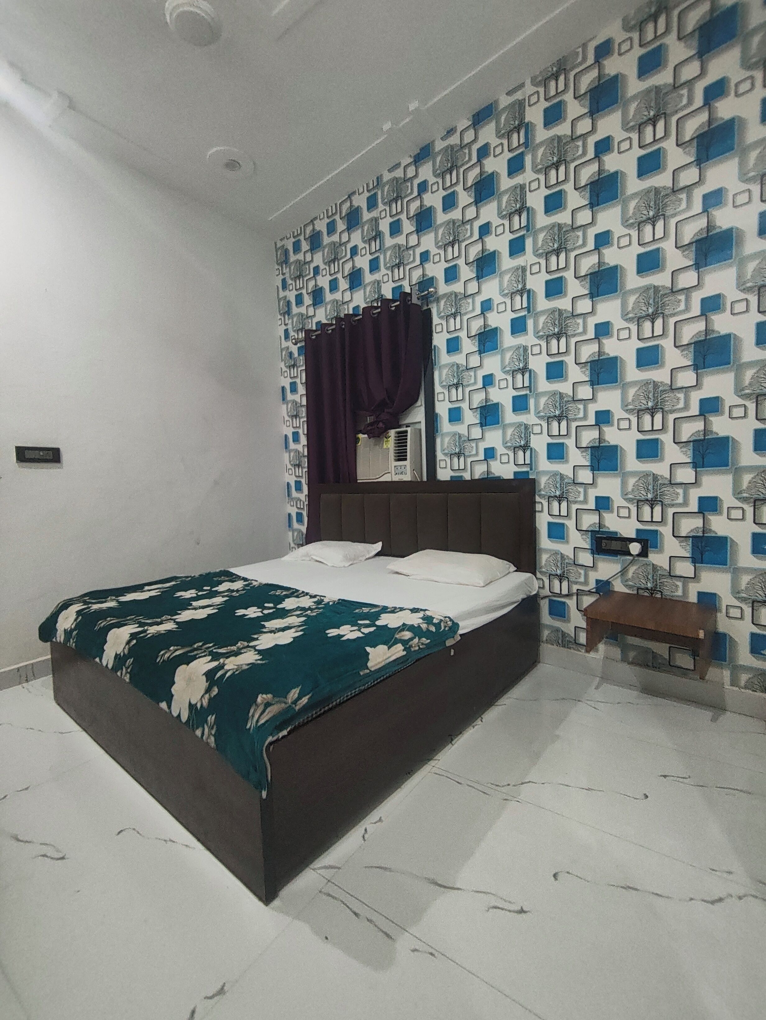 A bedroom with a bed, a nightstand, a wall-mounted air conditioner, and a patterned wallpaper.