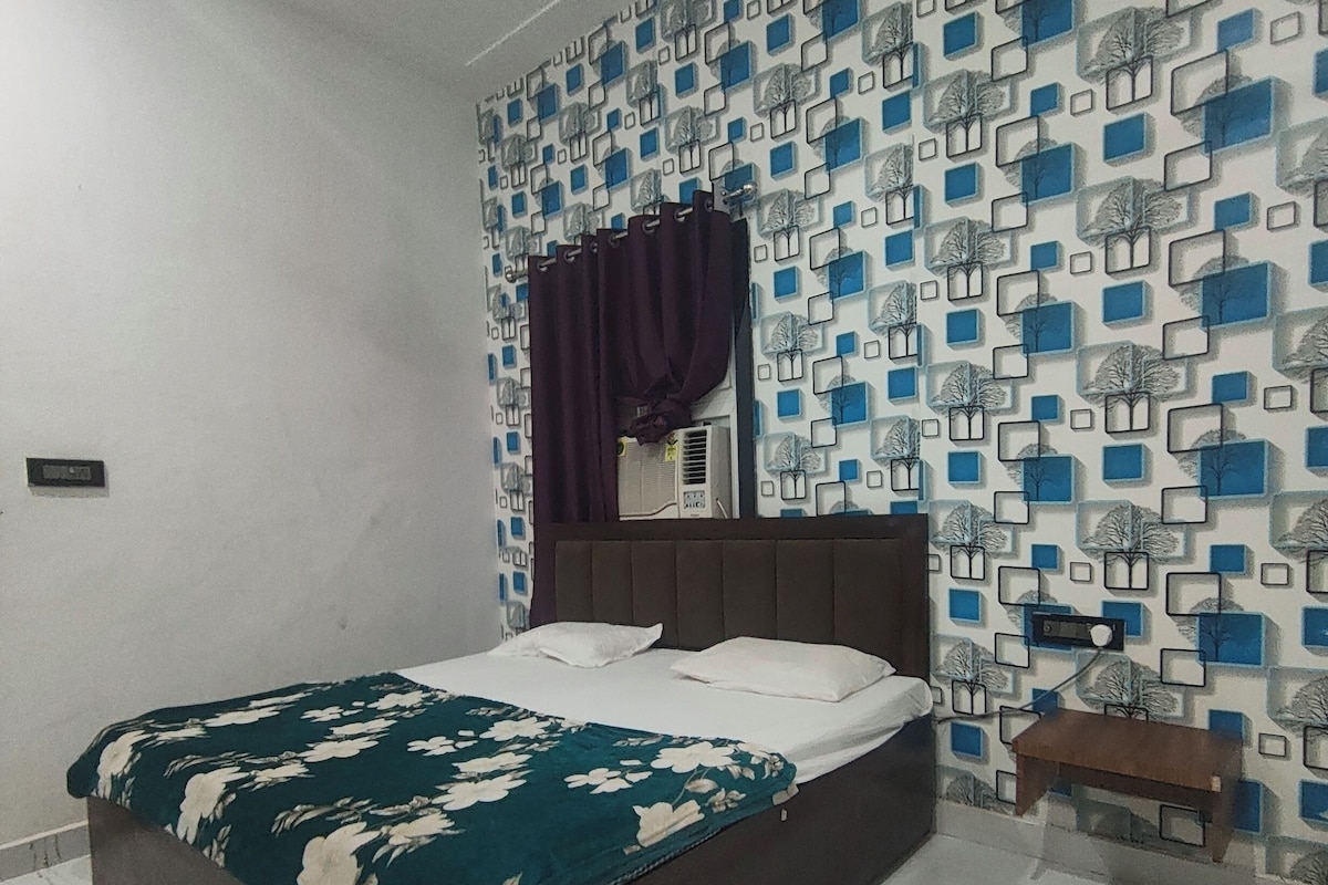 A bedroom with a bed, a nightstand, a wall-mounted air conditioner, and a patterned wallpaper.
