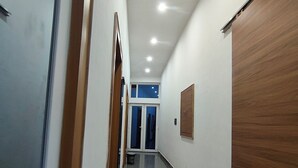 A hallway with a wooden door on the right, a blue door at the end, and a mat on the floor. - Hotel Town Inn Near Railway Station (Mathura)