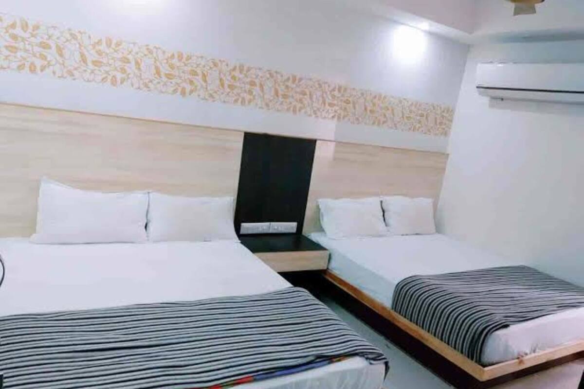 Habitación de hotel con dos camas, cabecera con diseño de hojas y un equipo de aire acondicionado.