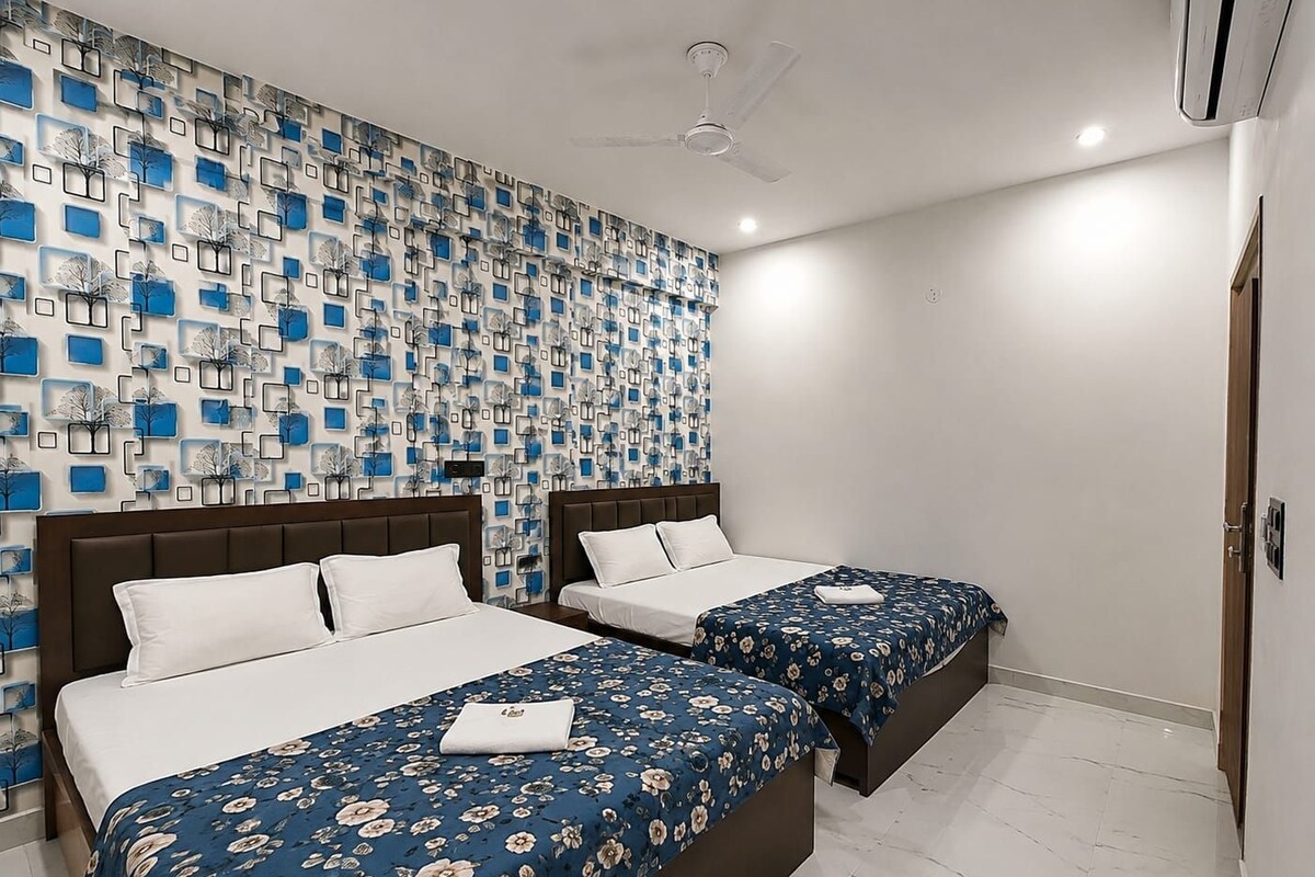 A hotel room with two beds, a patterned wall, a ceiling fan, and a white floor.