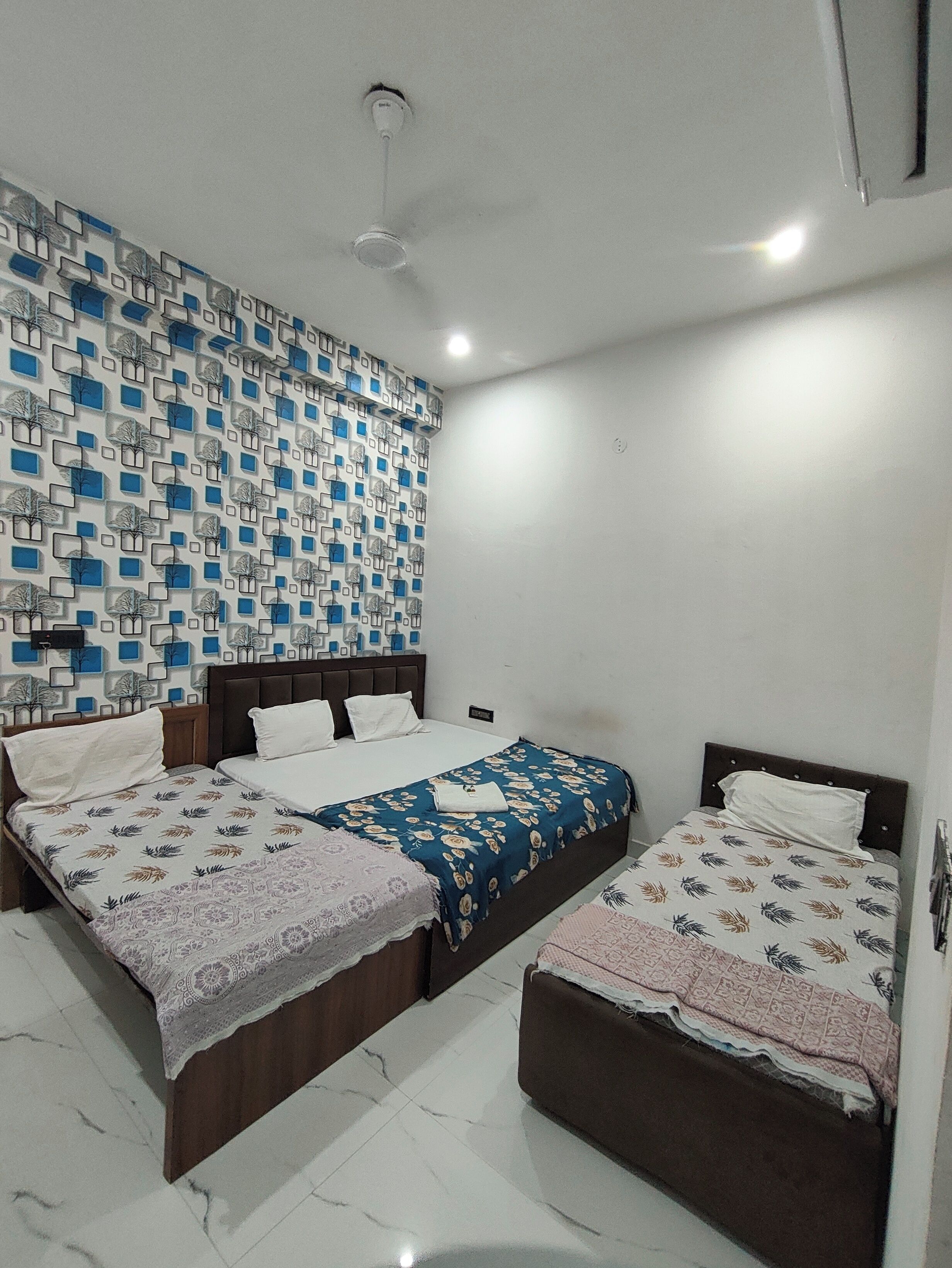 Quarto com duas camas, papel de parede estampado e ventoinha no teto.