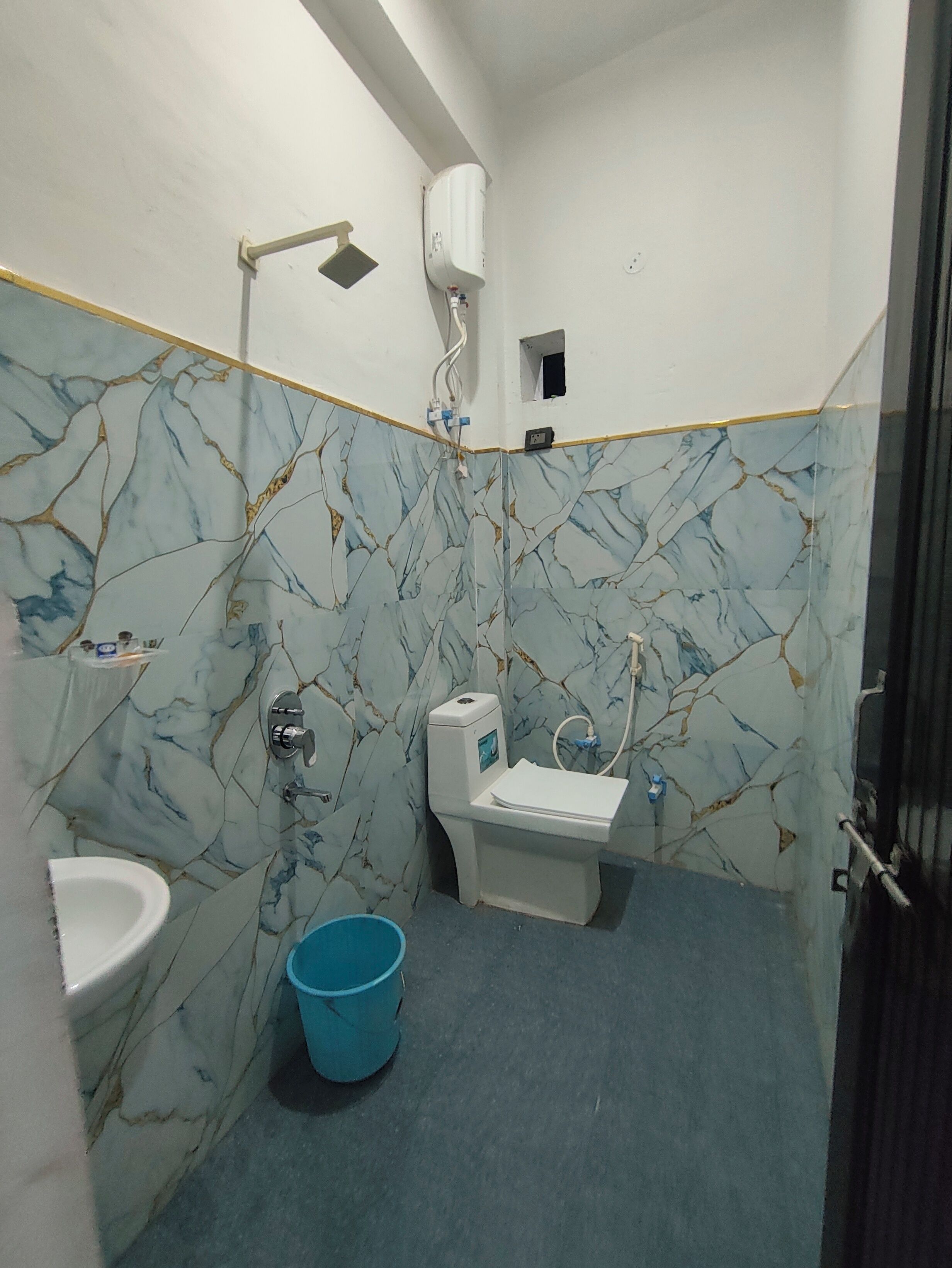 A bathroom with a toilet, sink, and a blue bucket on the floor.