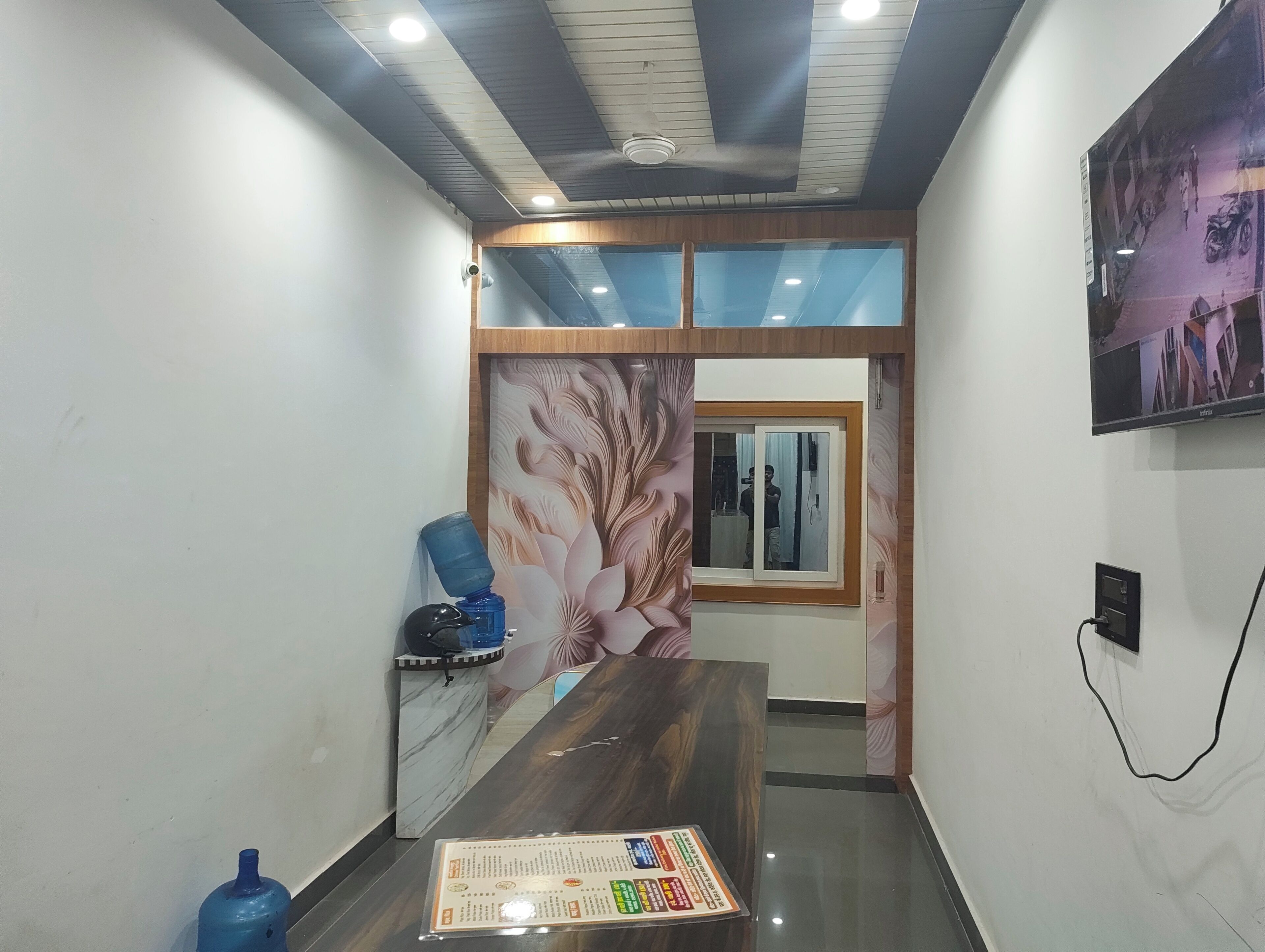 A hotel lobby with a reception desk, a large mirror, and a wall-mounted television.