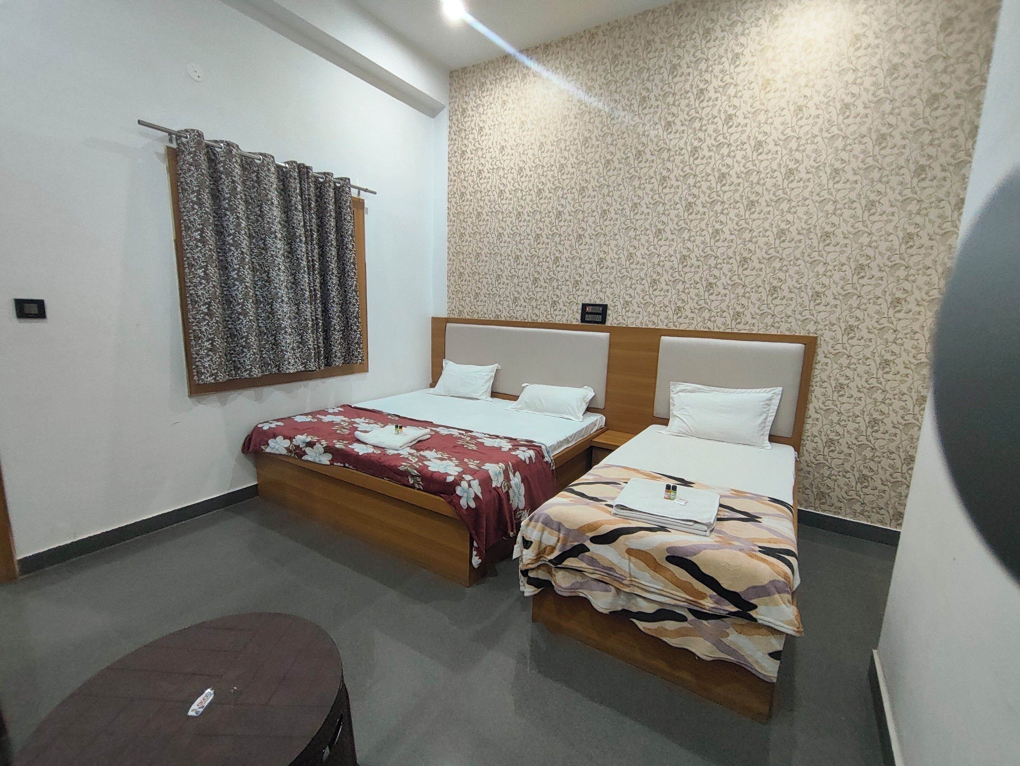 A hotel room with two beds, a small table, and a patterned wall.