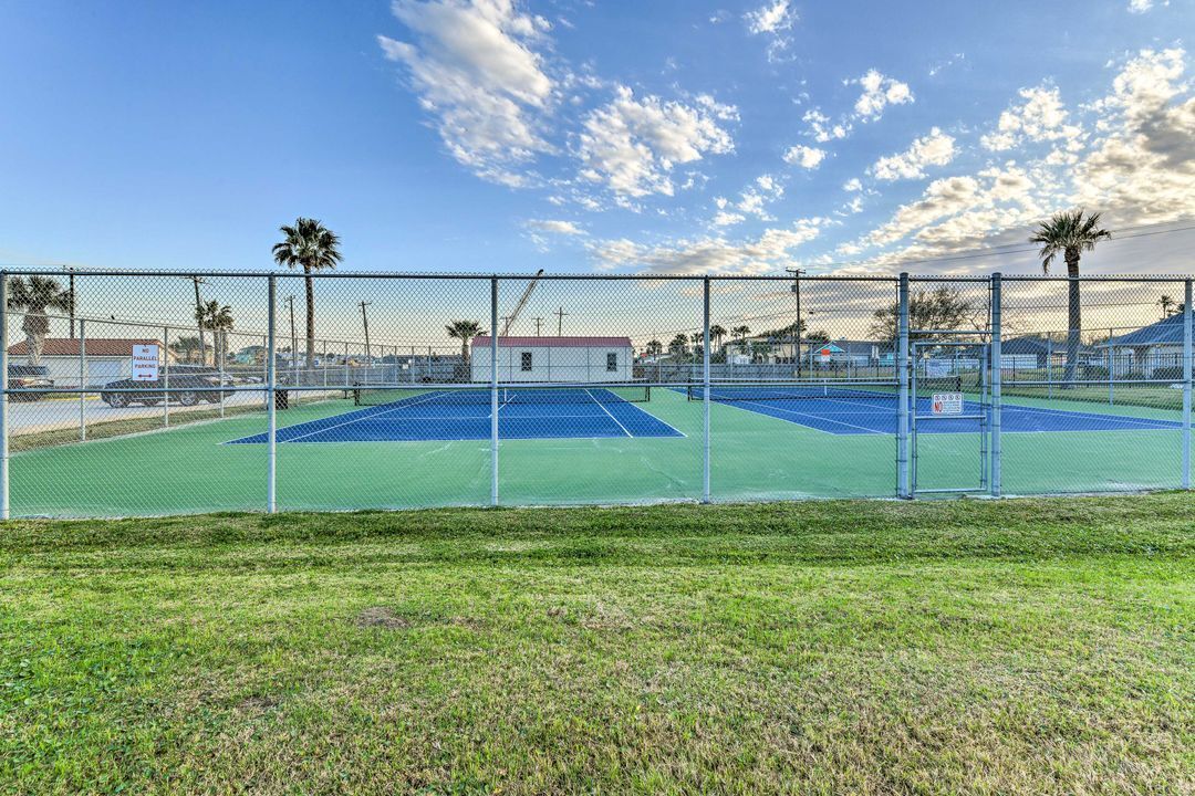 A tennis court enclosed by a chain-link fence with a small building in the background.