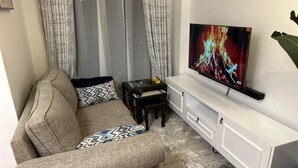 Een woonkamer met een bank, een salontafel, een tv op een witte kast en gordijnen.