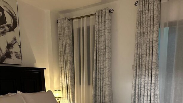 Een slaapkamer met een groot bed, witte beddengoed, een pluizig wit vloerkleed en een verwarming op de vloer.