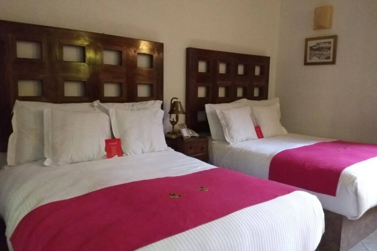 Dos camas individuales con cabeceros de madera, ropa de cama blanca y mantas rosas.