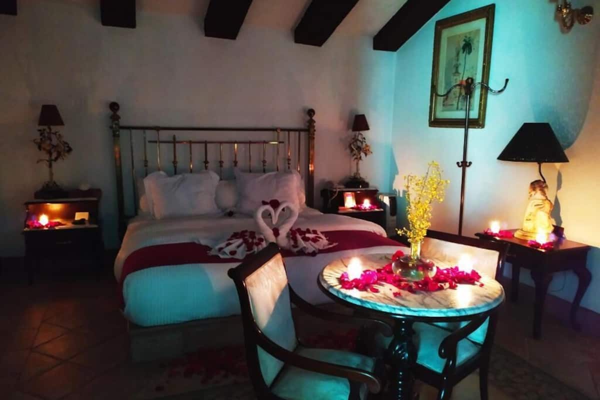 Un dormitorio con cama, mesitas de noche, una mesa redonda con un jarrón y flores, y una silla.