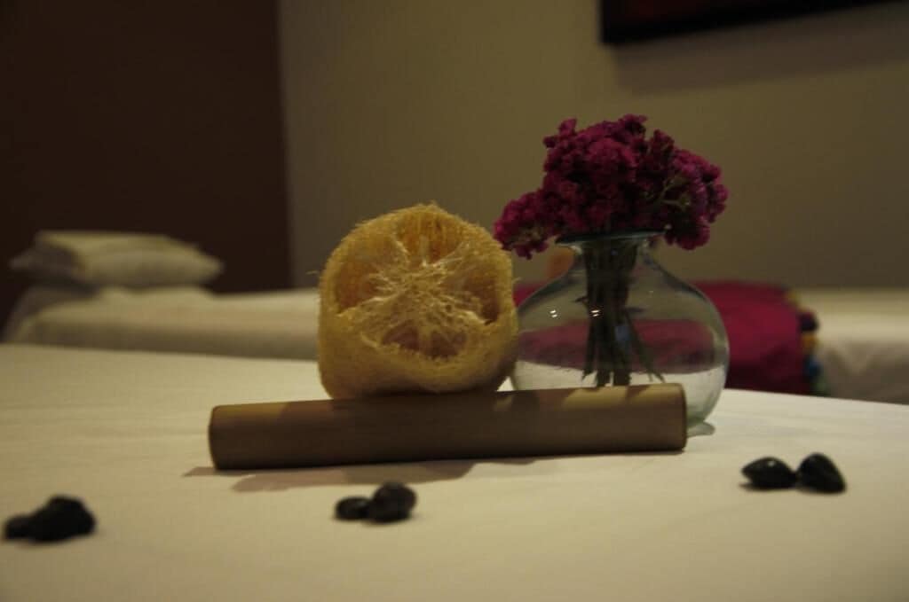 A bed with a rolled towel, a half-cut orange, a vase with flowers, and scattered berries.