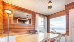 Ein Zimmer mit Holzwänden, einem großen Tisch, Stühlen, einem Spiegel und Meerblick.
