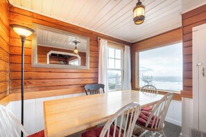 Ein Zimmer mit Holzwänden, einem großen Tisch, Stühlen, einem Spiegel und Meerblick.