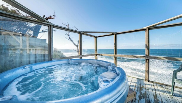Ein Whirlpool mit Holzterrasse und Glasumrandung mit Blick auf den Ozean.