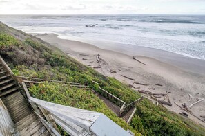 Eine Holztreppe führt hinunter zu einem Strand, im Hintergrund sind Wellen zu sehen.