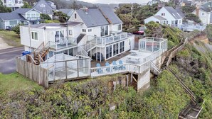 Ein Küstenhaus mit einem verglasten Wintergarten, einer Holzterrasse und einer Treppe, die zum Obergeschoss führt.