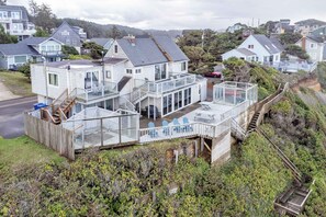 Ein Küstenhaus mit einem verglasten Wintergarten, einer Holzterrasse und einer Treppe, die zum Obergeschoss führt.