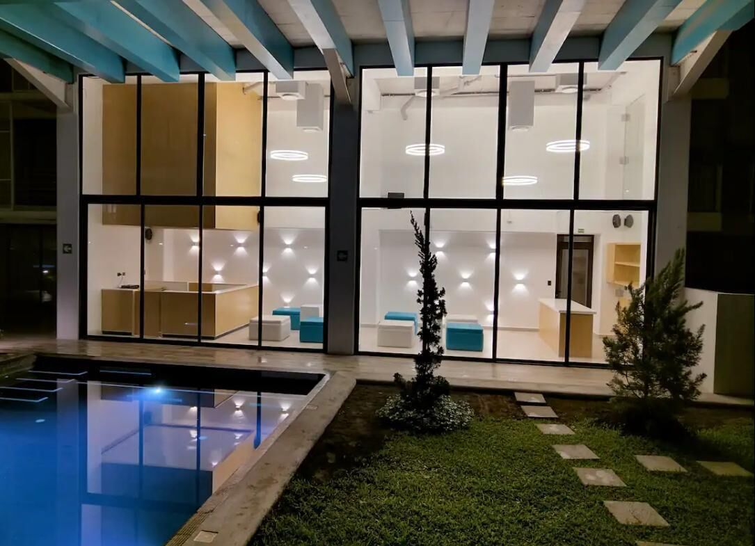 Um edifício moderno com fachada de vidro, piscina e um jardim bem cuidado.