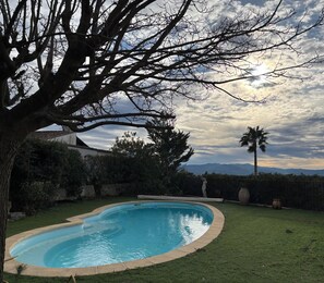 Un giardino con piscina, una palma e vista sulle montagne.
