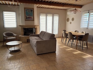 Un salon avec une cheminée, un canapé, une table à manger avec des chaises et un plafond avec des poutres en bois.