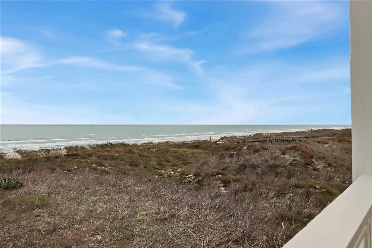 A coastal view with a beach, grassy terrain, and a wooden walkway.