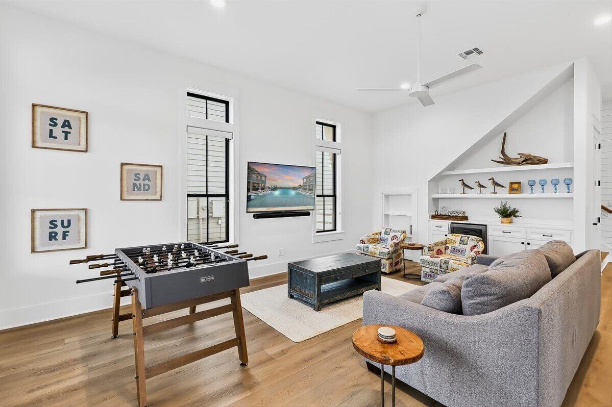 A modern living room with a foosball table, a grey sofa, a coffee table, and a TV on the wall.